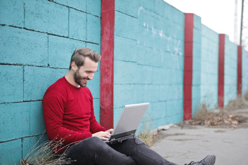 man-leaning-against-wall-using-laptop-941572.jpg